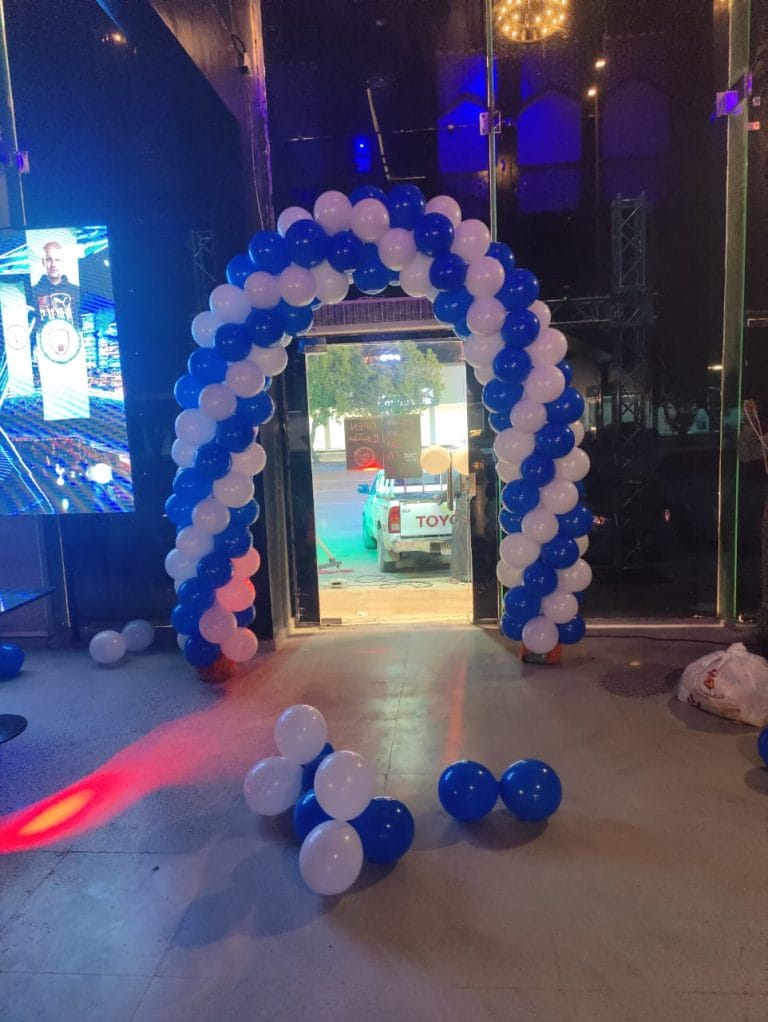 قوس بالونات أزرق وأبيض عند مدخل محل مع إضاءة زرقاء ليلًا