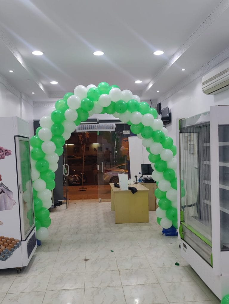 قوس بالونات أخضر وأبيض عند مدخل محل في يوم الافتتاح